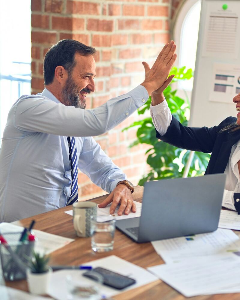 Two Hook Consulting advisors celebrating with a high five at a shared desk