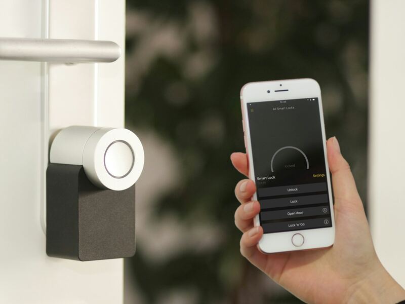 A hand holding a phone beside a smart lock on a front door